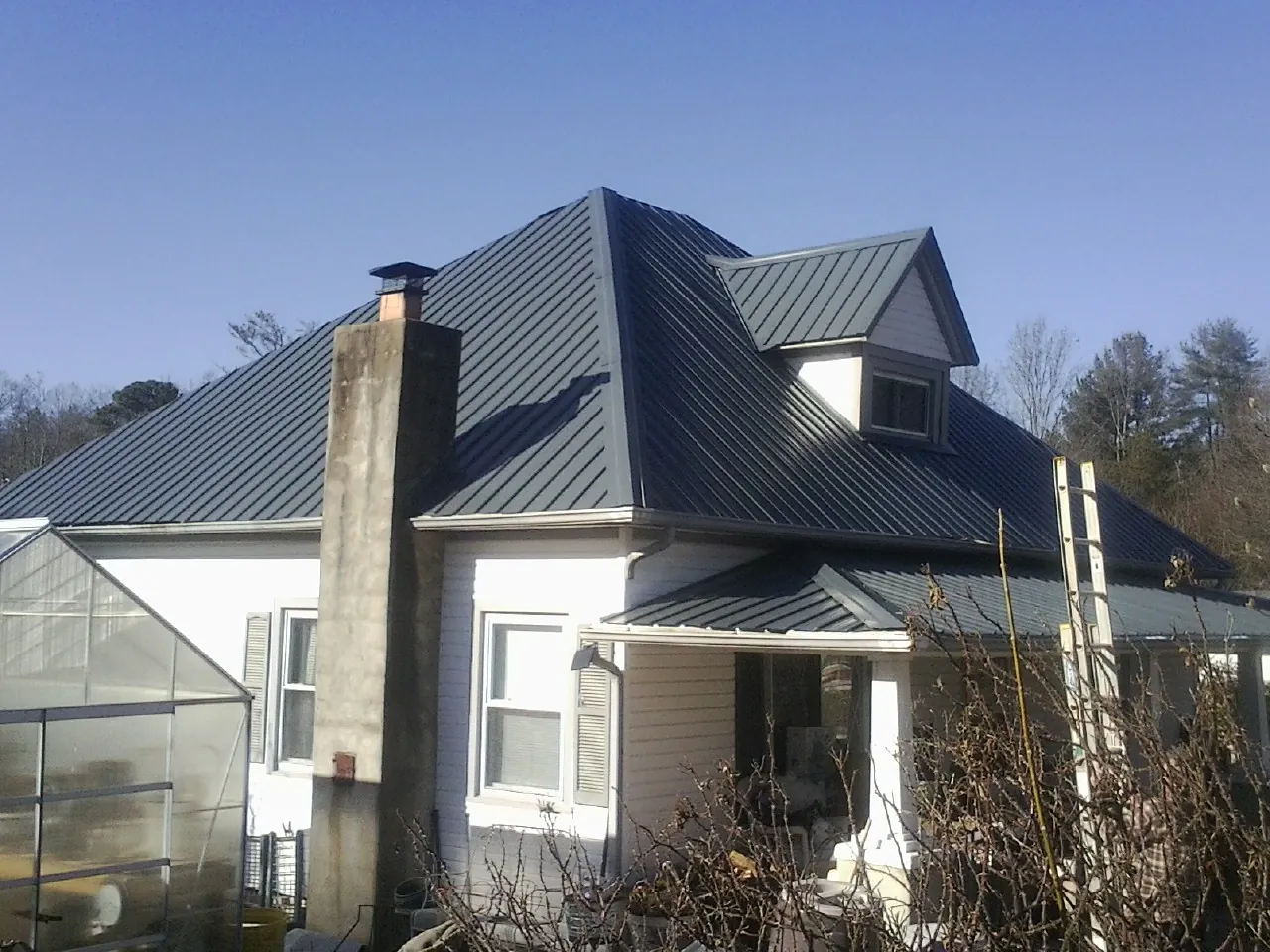 Dark blue standing seam metal roof on a white farmhouse with dormer — Slate & Tile Roof Repair by Roofing Brothers in Rumford