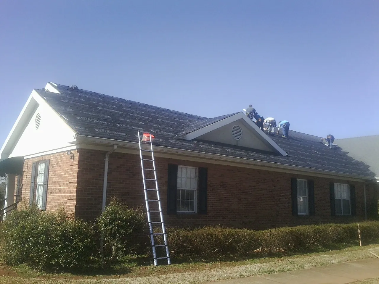 Crew tearing shingles off a brick ranch roof with a ladder set — Emergency Roof Repair work by our crew in Rumford