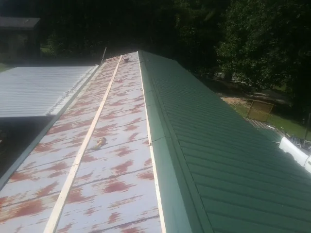 Old rusted panels beside newly installed green metal roofing — Wind Damage Roof Repair by Roofing Brothers in Rumford