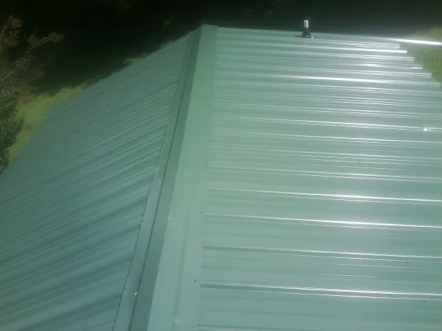 New green metal panels meeting at the ridge of a roof — Flat Roof Repair work by our crew in Rumford