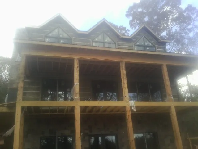 Dormers and porch framing on a large log home under construction — Roof Coating work by our crew in Rumford