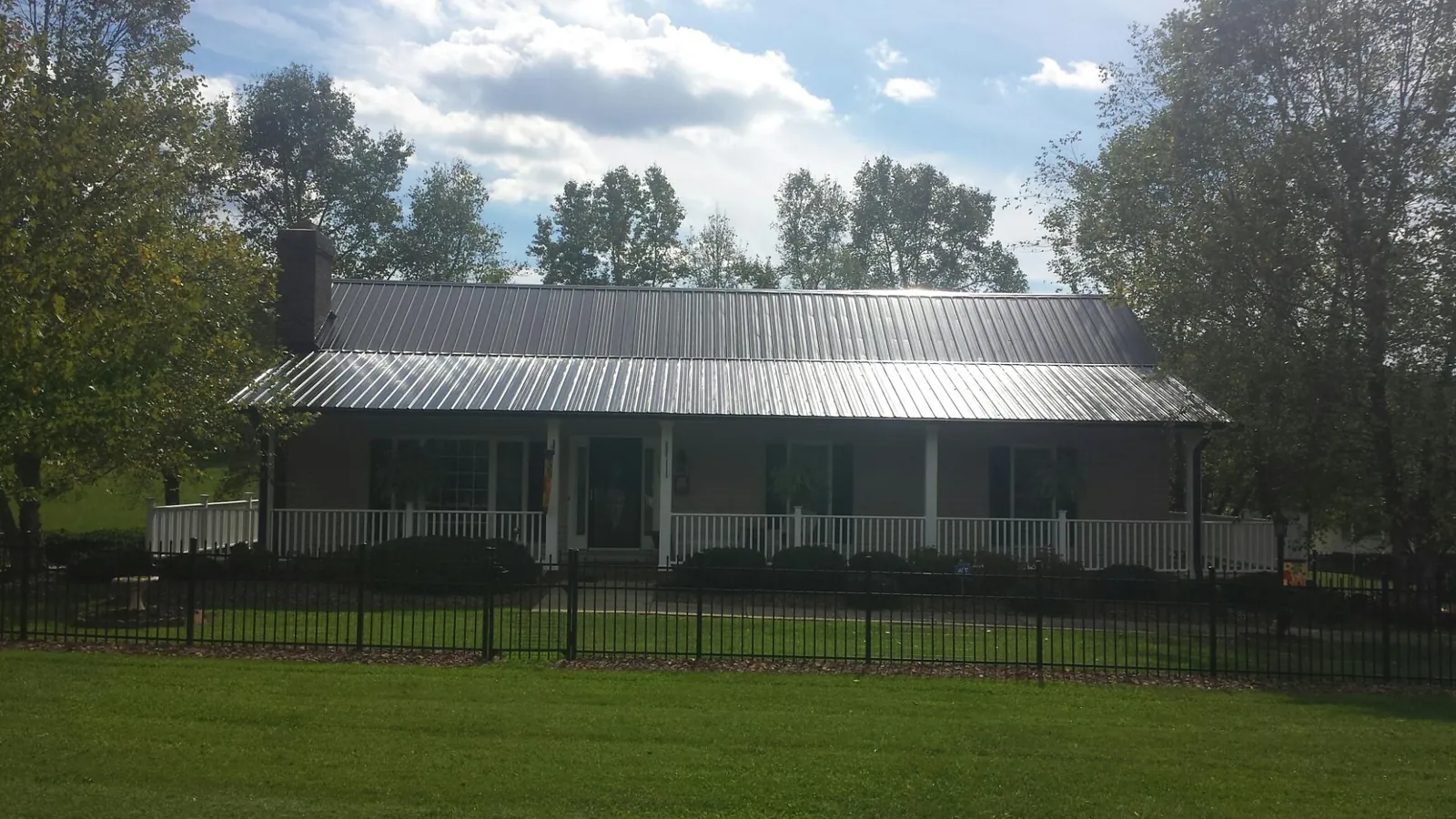Gray metal roof on a brick ranch with a full width front porch — Gutter Guard Installation work by our crew in Rumford
