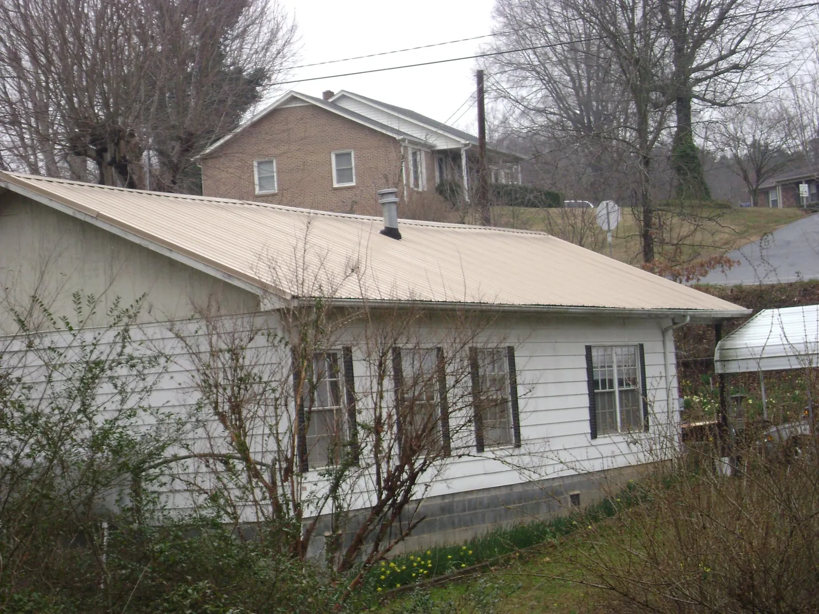 Tan metal roof on a white sided house set into a hillside — Commercial Roofing by Roofing Brothers in Rumford