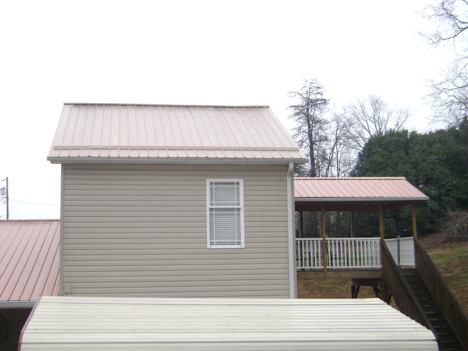 Tan metal roofs on a two story addition and attached porch, from a Roof Replacement job in Rumford